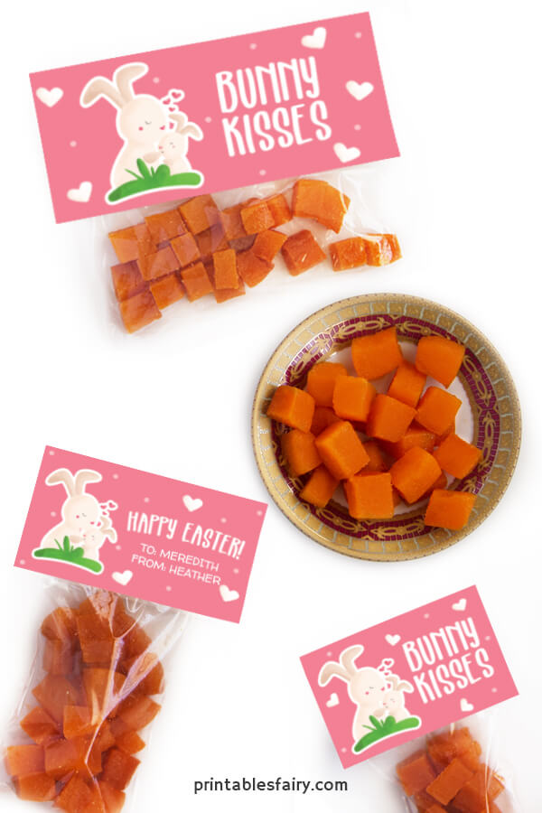 Bags of orange gummies with pink toppers that read happy Easter next to an illustration of bunnies kissing