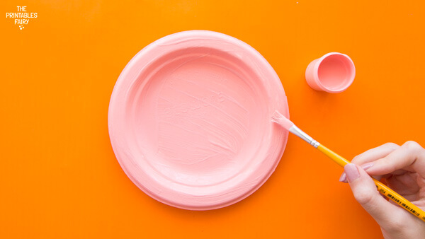 Painting a paper plate with pink tempera paint