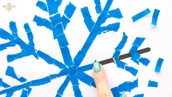 Gluing blue paper scraps on the snowflake outline