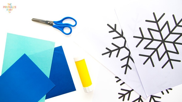 From left to right: blue paper scraps, scissors, glue stick, and snowflake templates