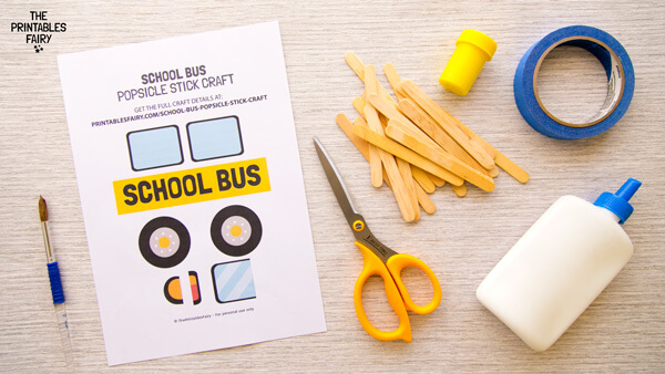 White table with the School Bus Printable, scissors, tape, glue, yellow paint, paintbrush, and popsicle sticks.