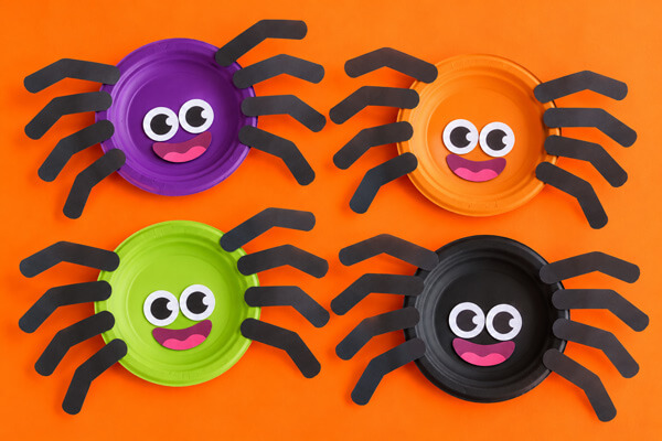 Orange table with paper plate spiders of different colors: purple, orange, green and black