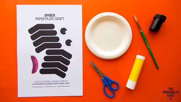 Orange table with the Spider Paper Plate Craft Template next to a paper plate, scissors, glue, black paint, and a paintbrush